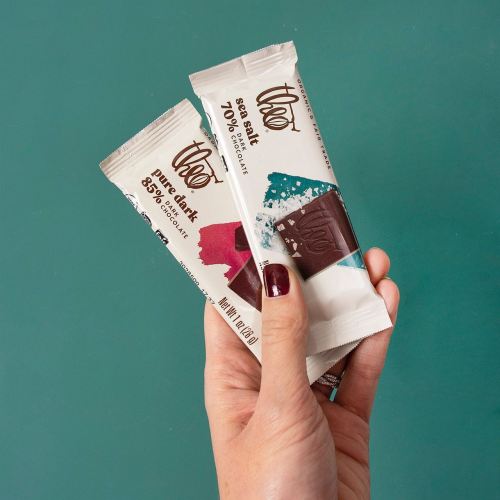 A hand holding two bars of Theo chocolate, one 70% dark and one 85% dark, against a teal background.