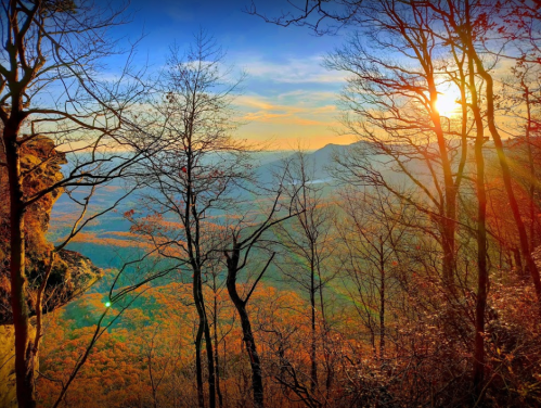 Sunset over a mountainous landscape, framed by bare trees and vibrant autumn foliage.