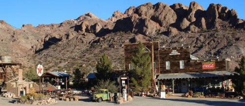 A rustic old town with wooden buildings and a vintage truck, set against a backdrop of rocky mountains.