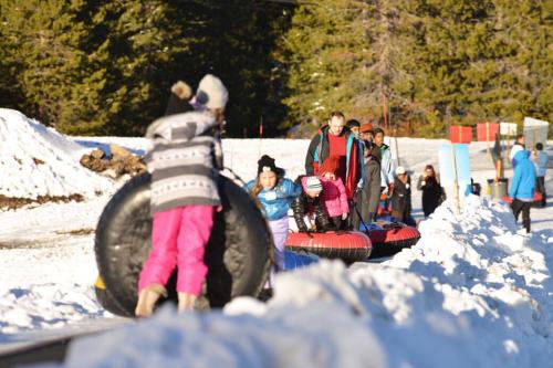People enjoying a snowy tubing area, pulling inflatable tubes along a snowy path with trees in the background.