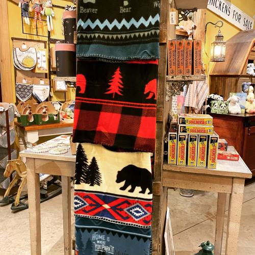 A display of patterned blankets featuring wildlife and nature themes in a cozy shop setting.