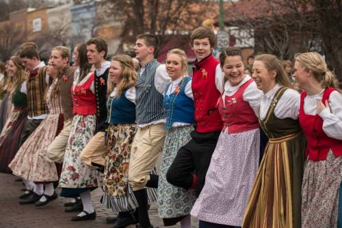 A group of young people in traditional costumes dancing together in a festive outdoor setting.