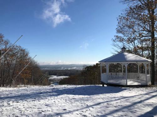 A snowy landscape with a white gazebo overlooking a valley under a clear blue sky.