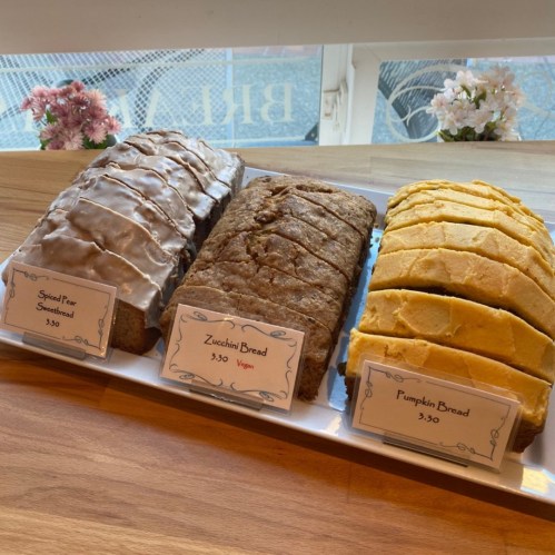 Three loaves of bread: spiced pear sweetbread, zucchini bread (vegan), and pumpkin bread, displayed on a white platter.