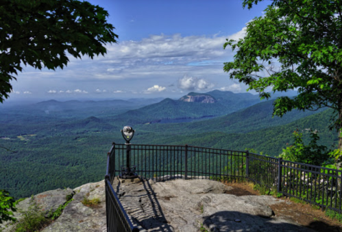 Scenic mountain view from a lookout point, featuring lush green valleys and distant peaks under a blue sky.