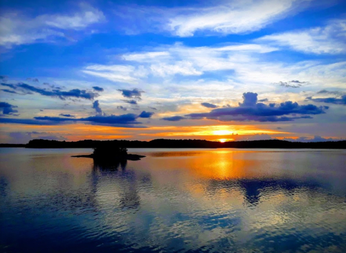 A serene lake at sunset, with vibrant colors reflecting on the water and clouds scattered across the sky.