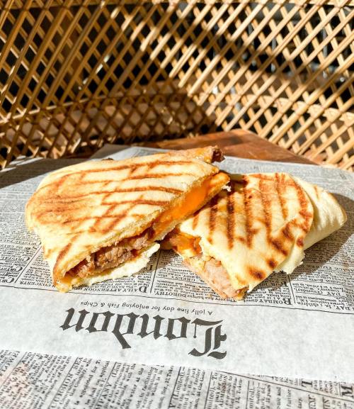 A grilled sandwich with melted cheese and meat, resting on newspaper-style wrapping in a warm, inviting setting.