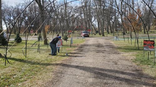 A person adjusts a sign under an archway in a park, with trees and a vehicle in the background.