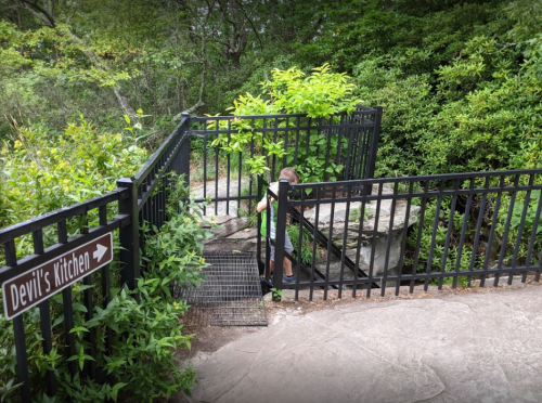 A child climbs a metal staircase leading to a fenced area marked "Devil's Kitchen," surrounded by greenery.