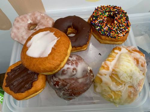 A variety of donuts on a tray, including glazed, chocolate, and sprinkles, arranged neatly.