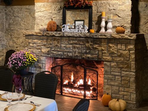 Cozy fireplace in a rustic setting, decorated with autumn decor and a "Thankful" sign, surrounded by pumpkins and flowers.