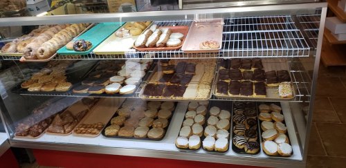 A display case filled with various baked goods, including cookies, pastries, and donuts, arranged on trays.