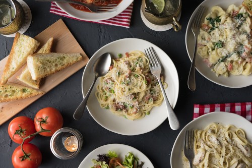 A table set with plates of pasta, garlic bread, fresh tomatoes, and a salad, creating a cozy dining atmosphere.