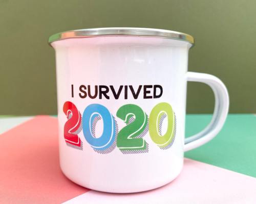 A white enamel mug with the text "I Survived 2020" in colorful letters against a green and pink background.