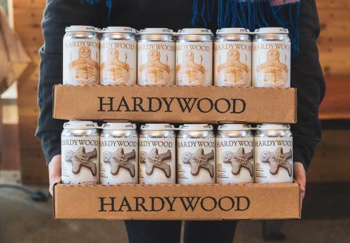 A person holds two boxes of Hardywood beer cans, stacked with a total of twelve cans featuring a gingerbread design.
