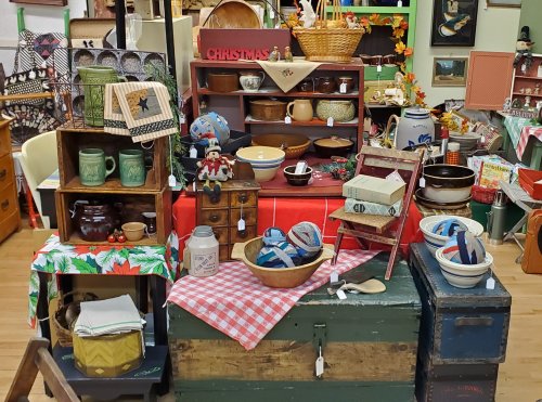 A vintage display featuring various antique kitchenware, baskets, and holiday decorations on a table.