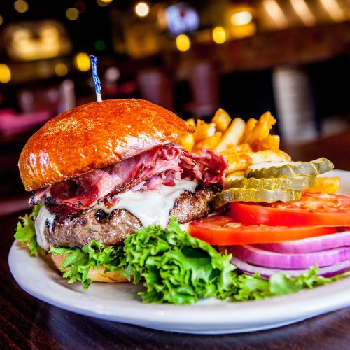 A juicy burger with melted cheese, roast beef, lettuce, tomato, pickles, and onion, served with crispy fries on the side.