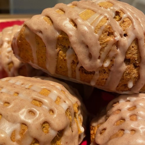 Close-up of freshly baked scones drizzled with a creamy glaze, arranged on a red plate.