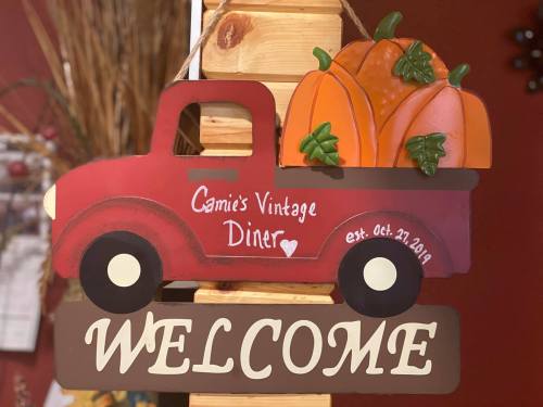 A red vintage truck sign with pumpkins in the back, reading "Gamie's Vintage Diner" and "Welcome."