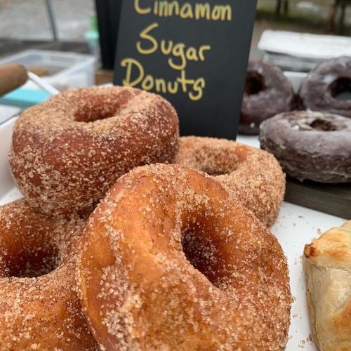 A close-up of cinnamon sugar donuts on a plate, with a chalkboard sign in the background.