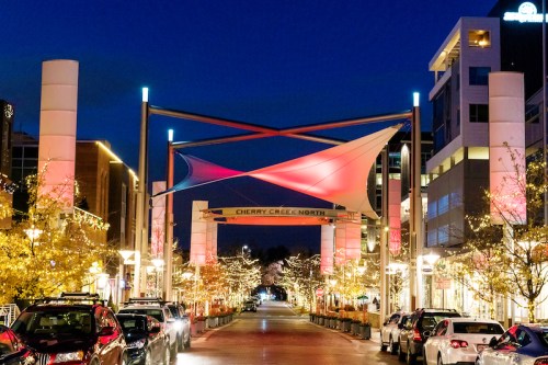 A vibrant night scene of Cherry Creek North, featuring illuminated trees and colorful canopies over a bustling street.