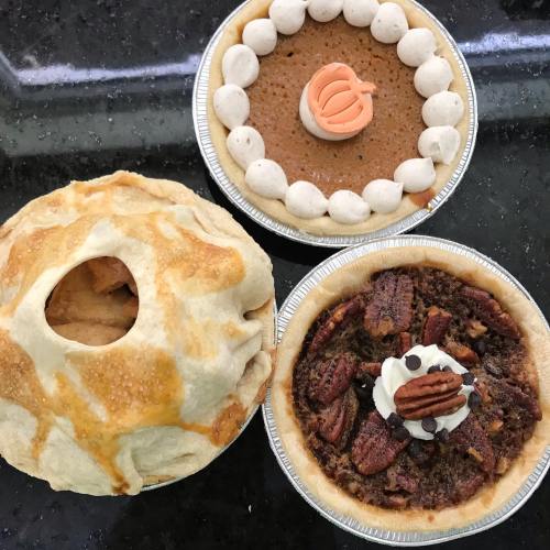 Three delicious pies: a pumpkin pie, a pecan pie with whipped cream, and a decorative apple pie.