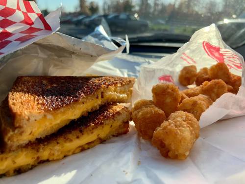 A grilled cheese sandwich with melted cheese and crispy tater tots on a car dashboard, with sunlight shining in.