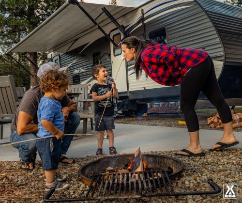 A family enjoys a camping trip, roasting marshmallows over a fire near their trailer, sharing smiles and laughter.