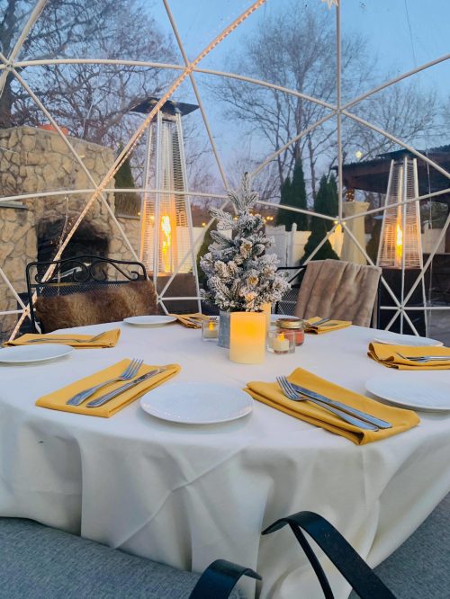 A cozy dining setup in a geodesic dome, featuring a festive centerpiece, candles, and neatly arranged tableware.