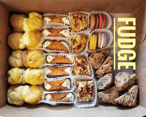 A box filled with assorted desserts: cream puffs, cannoli, macarons, fudge, and other sweet treats.