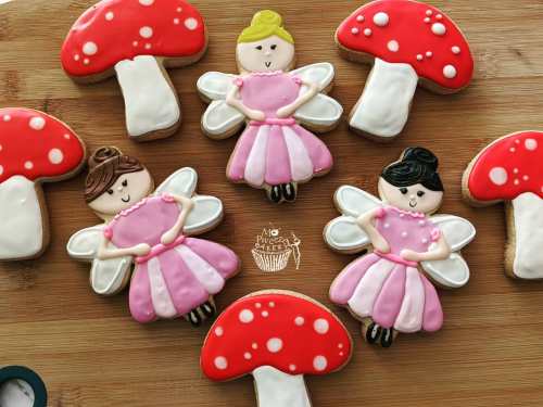 Colorful cookies shaped like fairies and mushrooms, decorated with icing on a wooden surface.