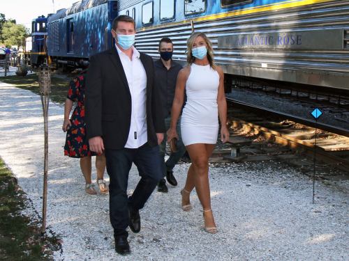 A group of people walking along a path near a train, wearing masks and dressed for an event.