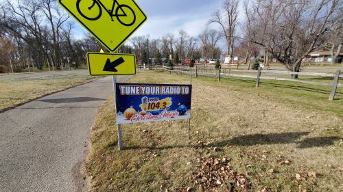 Sign directing to tune radio to 104.3 for Christmas music, with a bike lane sign in the background.