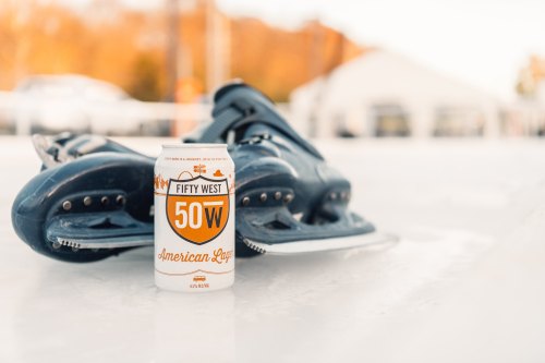 A can of Fifty West 50W American Lager sits on ice next to a pair of ice skates.