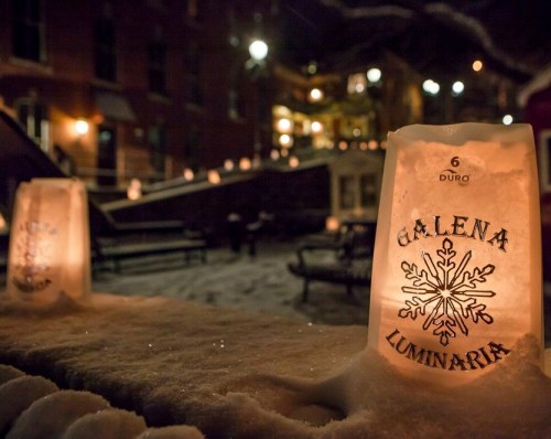 Luminaria bags glow softly in the snow, illuminating a winter scene in Galena at night.