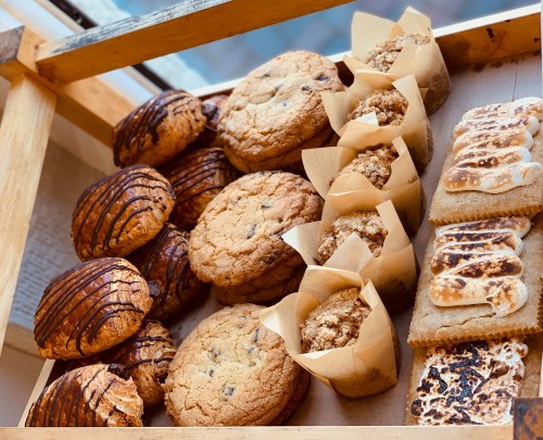 A display of assorted baked goods, including cookies, muffins, and pastries, arranged on a wooden tray.