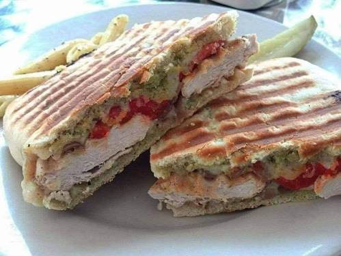 A grilled sandwich filled with chicken, roasted red peppers, and pesto, served with a side of pasta.