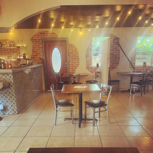 Cozy restaurant interior with brick walls, a bar, and tables set for dining under warm string lights.