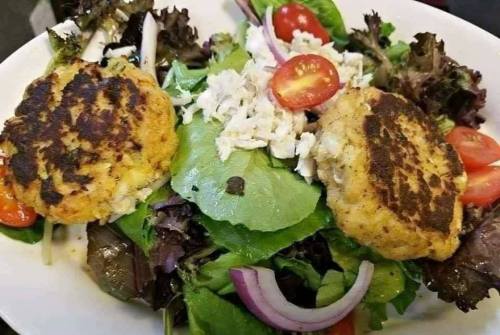 A fresh salad topped with two golden-brown patties, cherry tomatoes, and mixed greens.