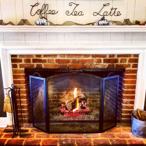 A cozy fireplace with a black screen, surrounded by a brick wall and a sign that reads "Coffee Tea Latte."