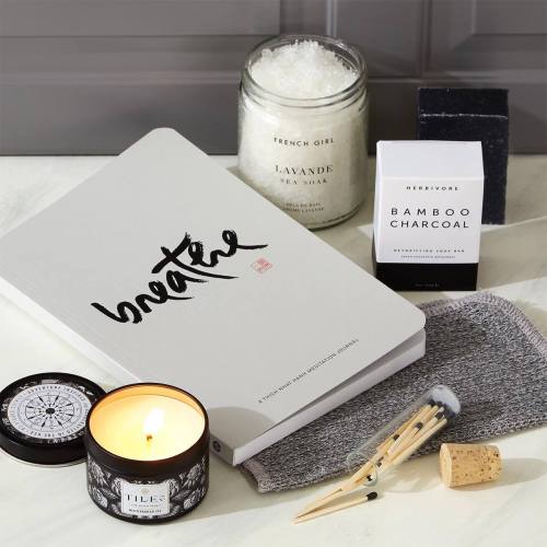 A serene flat lay featuring a journal, candle, charcoal soap, and bath accessories on a textured surface.