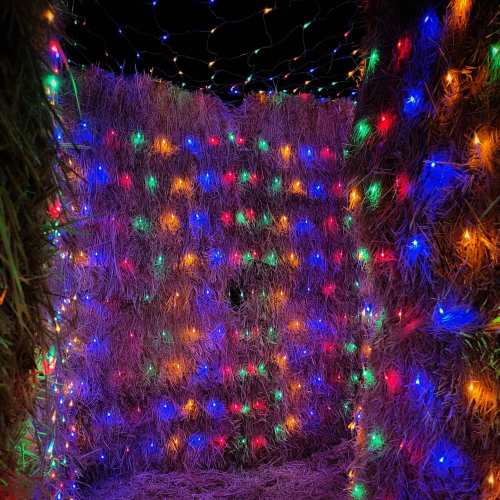 A colorful maze made of hay bales, illuminated with vibrant, multicolored lights.