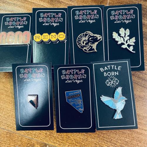 A collection of various pins displayed on black cards, featuring designs like "Reno," a ram, and a Nevada outline.