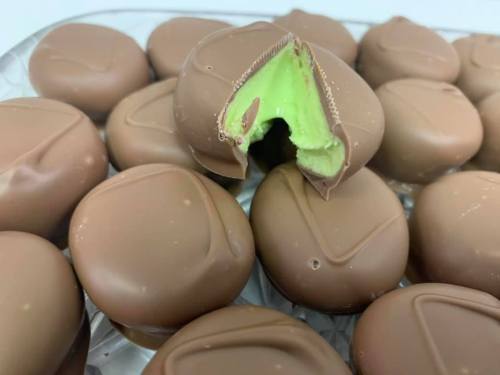 A close-up of chocolate-covered candies, with one cut in half to reveal a green mint filling inside.