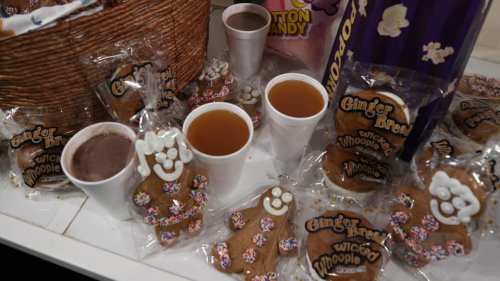 A table with gingerbread cookies, two cups of drink, and a basket of cotton candy.