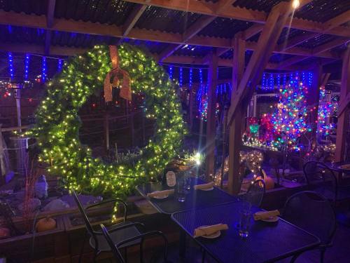 A festive outdoor dining area decorated with colorful Christmas lights, a large wreath, and a Christmas tree.