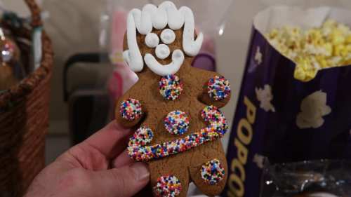 A hand holding a decorated gingerbread cookie with colorful sprinkles and icing, resembling a person.