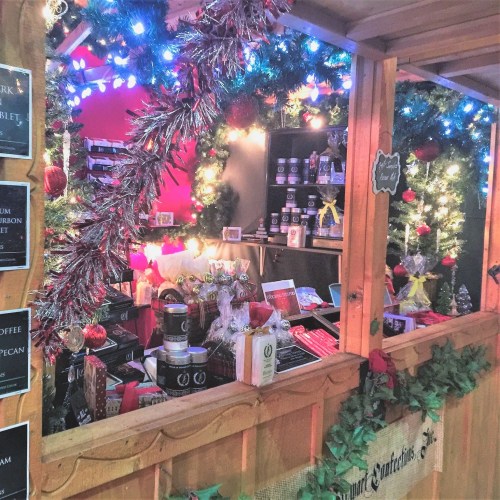 A festive market stall decorated with lights and garlands, displaying various holiday treats and gifts.