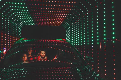 A family in a car surrounded by colorful lights in a festive tunnel at night.