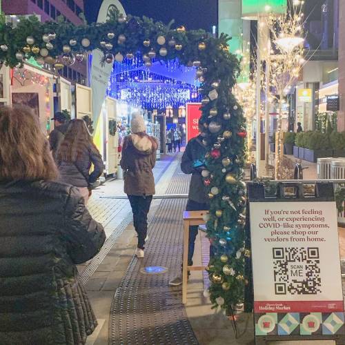 A festive archway decorated with greenery and ornaments leads to a market, with a sign about shopping from home.